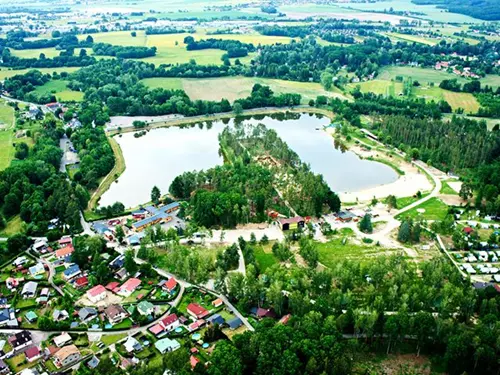 Vzdušný pohled na velký rybník s ostrovem a okolní vesnicí.