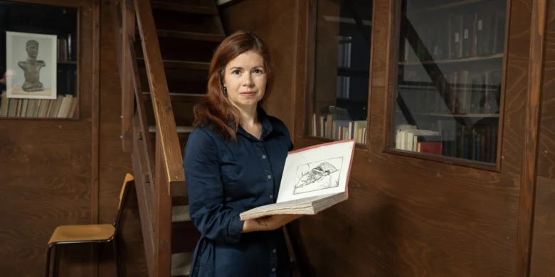 Žena drží otevřenou knihu v knihovně nebo archivu.