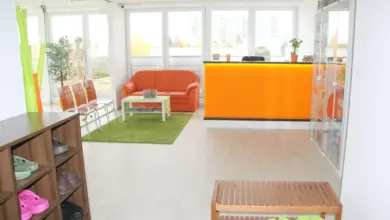 Moderní čekárna s oranžovou pohovkou a zelenou kobercem.