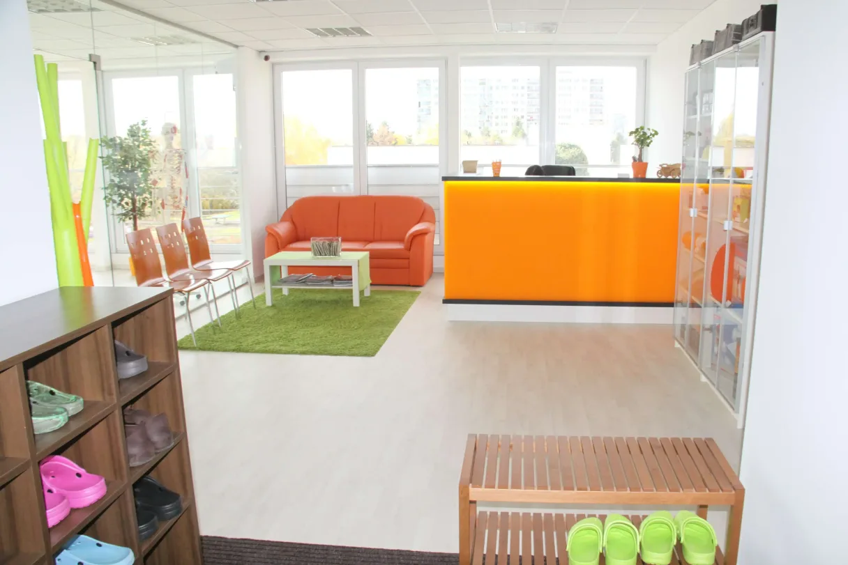 Moderní čekárna s oranžovou pohovkou a zelenou kobercem.