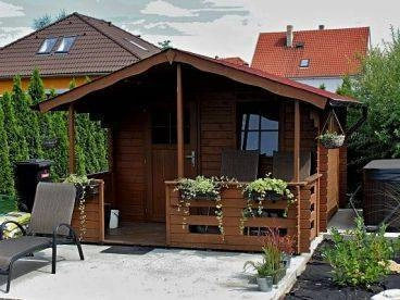 Hnědá dřevěná pergola s kvetoucími rostlinami v nádobách.