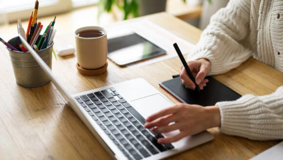 Osoba pracuje na počítači s digitálním tabletem u stolu.