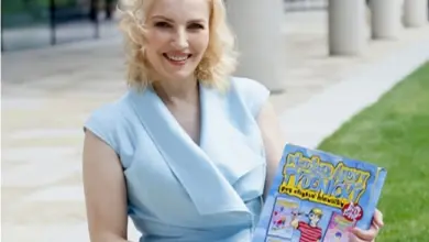 Žena drží dětskou anglickou knihu venku na trávníku.