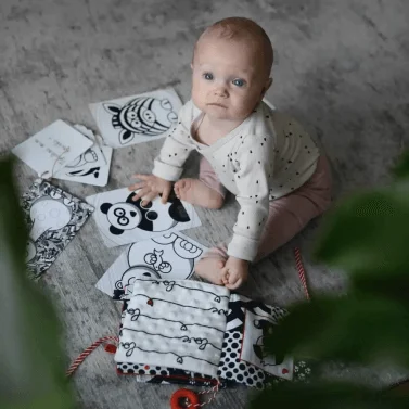 Béba sedí na podlaze s černobílými kartami kolem sebe.