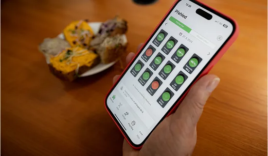 Ruka drží telefon s aplikací pro bezlepkovou stravu nad jídlem.