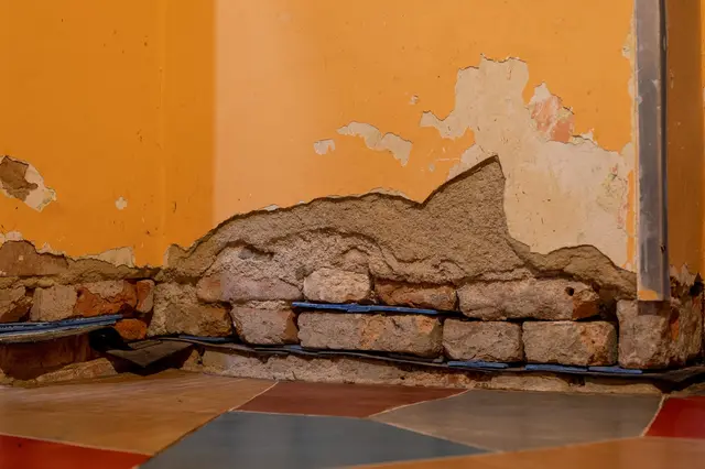 Poškozený roh stěny s odškrábnutým omítkou a viditelnými cívami.