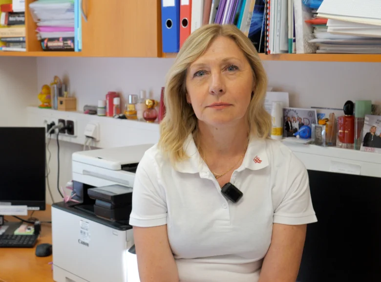 Žena sedí v kanceláři s tiskárnou a regály plnými dokumentů.