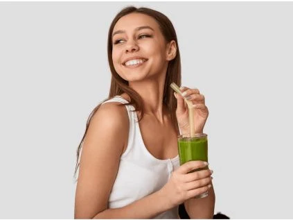Žena pije zelený džus, který může obsahovat vitamín B12.