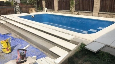 Nově postavený bazén s schody z pórobného betonu vedoucími do vody.