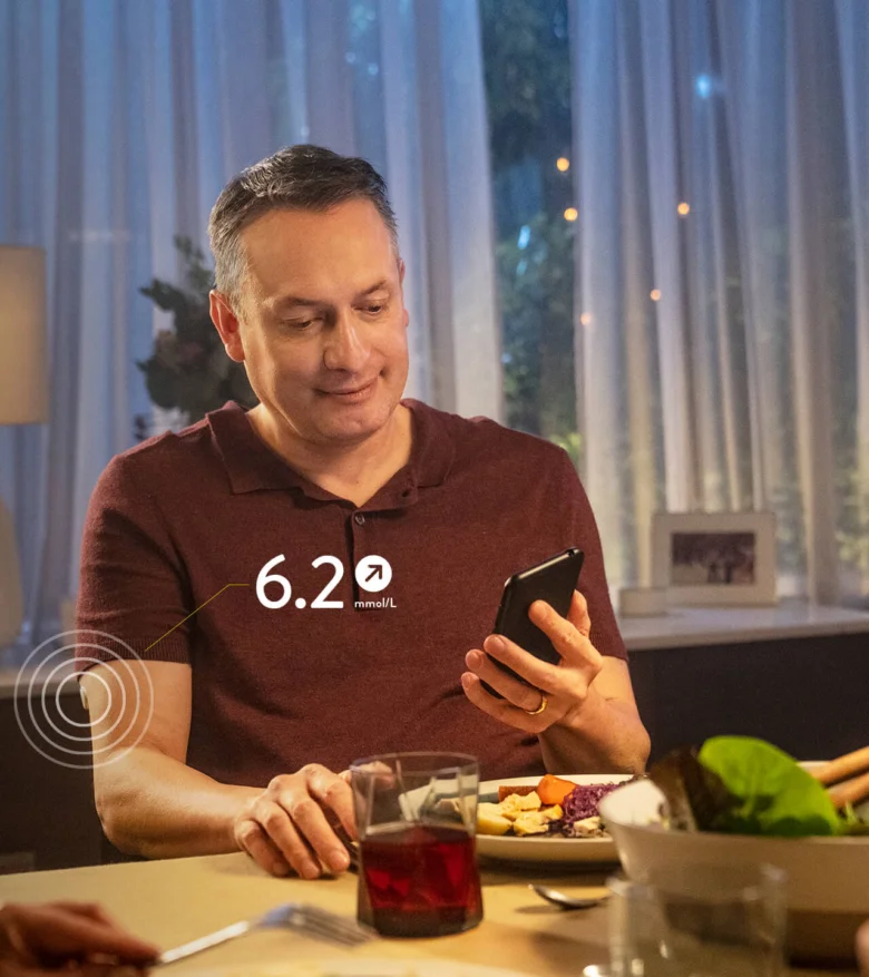 Muž sleduje svou hladinu cukru v krvi pomocí chytrého telefonu během večeře.