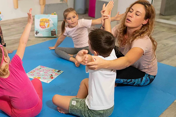 Dospělá žena vede děti v cvičení jógy na matracích.