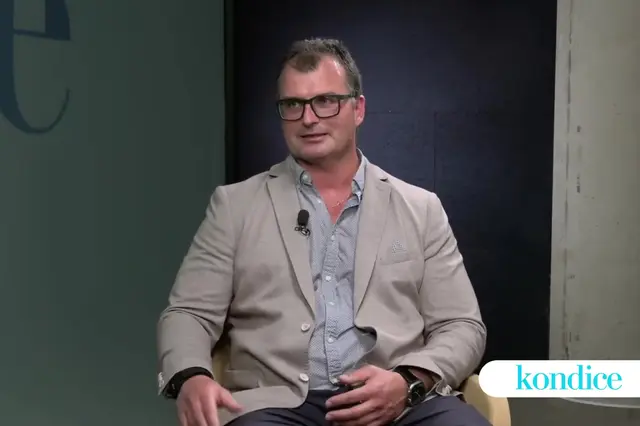 Muž s šedými vlasy v brýlích sedí na židli.