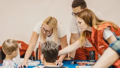 Dospělí v oranžových vestách ukazují dětem přístroj na stole.