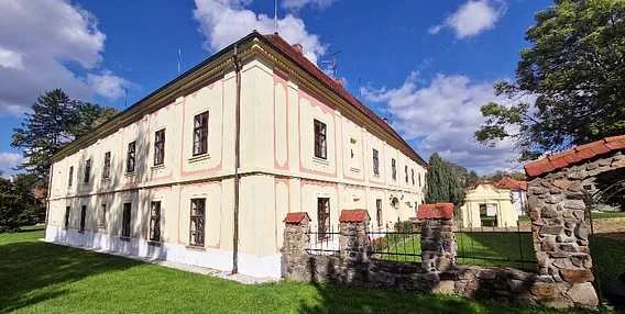 Historický zámek v Mikulčicích s červenou střechou na zelené trávě.