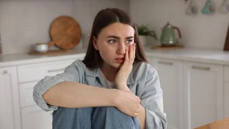 Žena sedí v kuchyni s výrazem strachu na obličeji.
