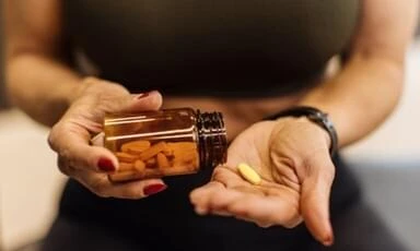 Osoba drží lahvičku s doplňky stravy a dvě žluté tobolky.