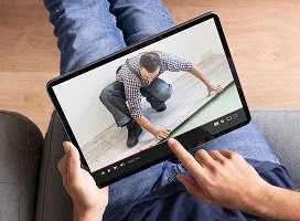 Muž pokládá vinylovou podlahu klečící na dřevěném povrchu.