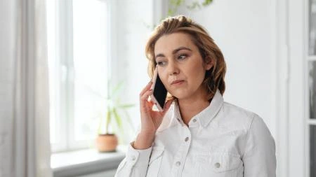 Žena mluví na telefonu v interiéru u okna.