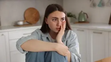 Žena sedí v kuchyni s výrazem bolesti nebo úzkosti.