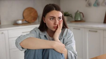 Žena sedí v kuchyni s výrazem starosti.